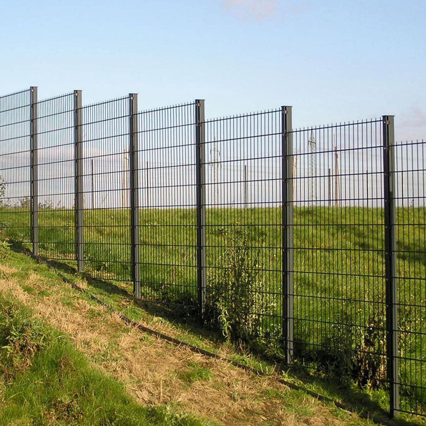 Panneaux grillagés rigides installés sur poteaux le long d’un terrain en pente.