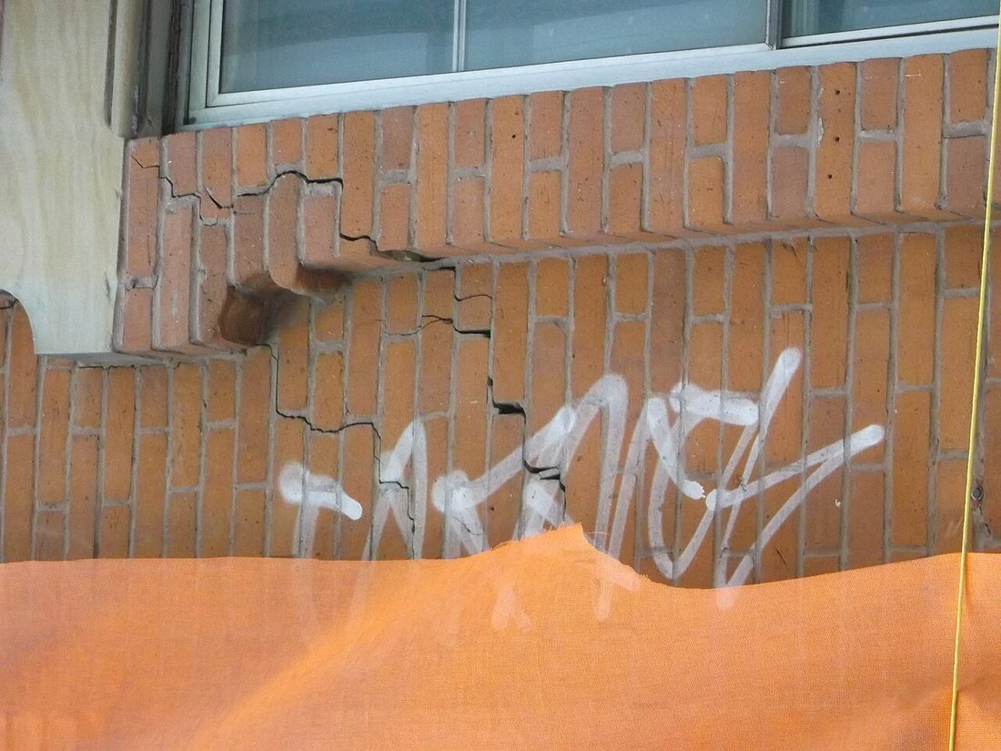 Fissure en escalier dans une façade de briques, près d’une fenêtre