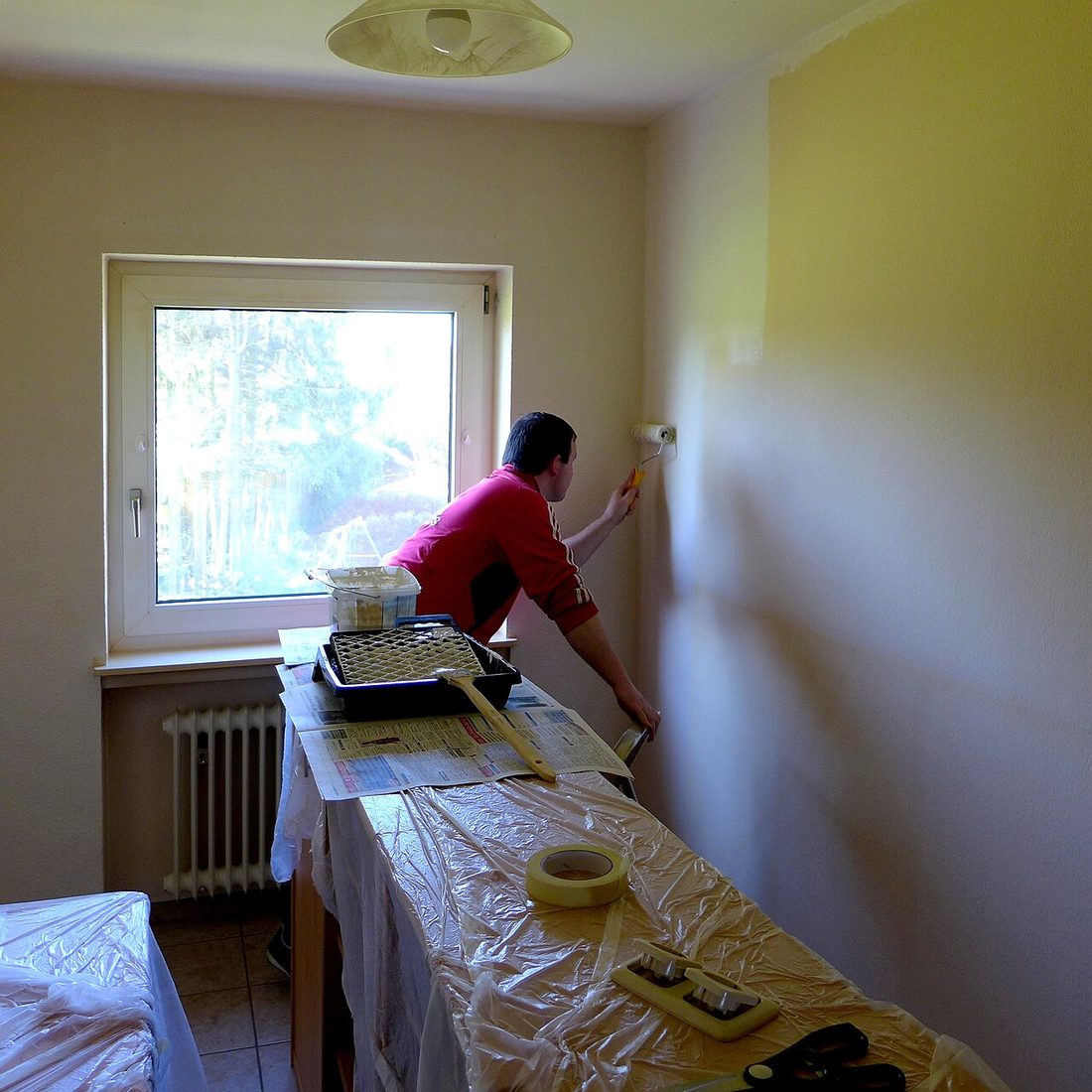 Personne appliquant de la peinture au rouleau sur un mur intérieur, avec les abords protégés