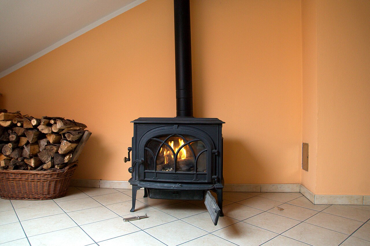 Poêle à bûches allumé avec porte vitrée et conduit vertical visible.