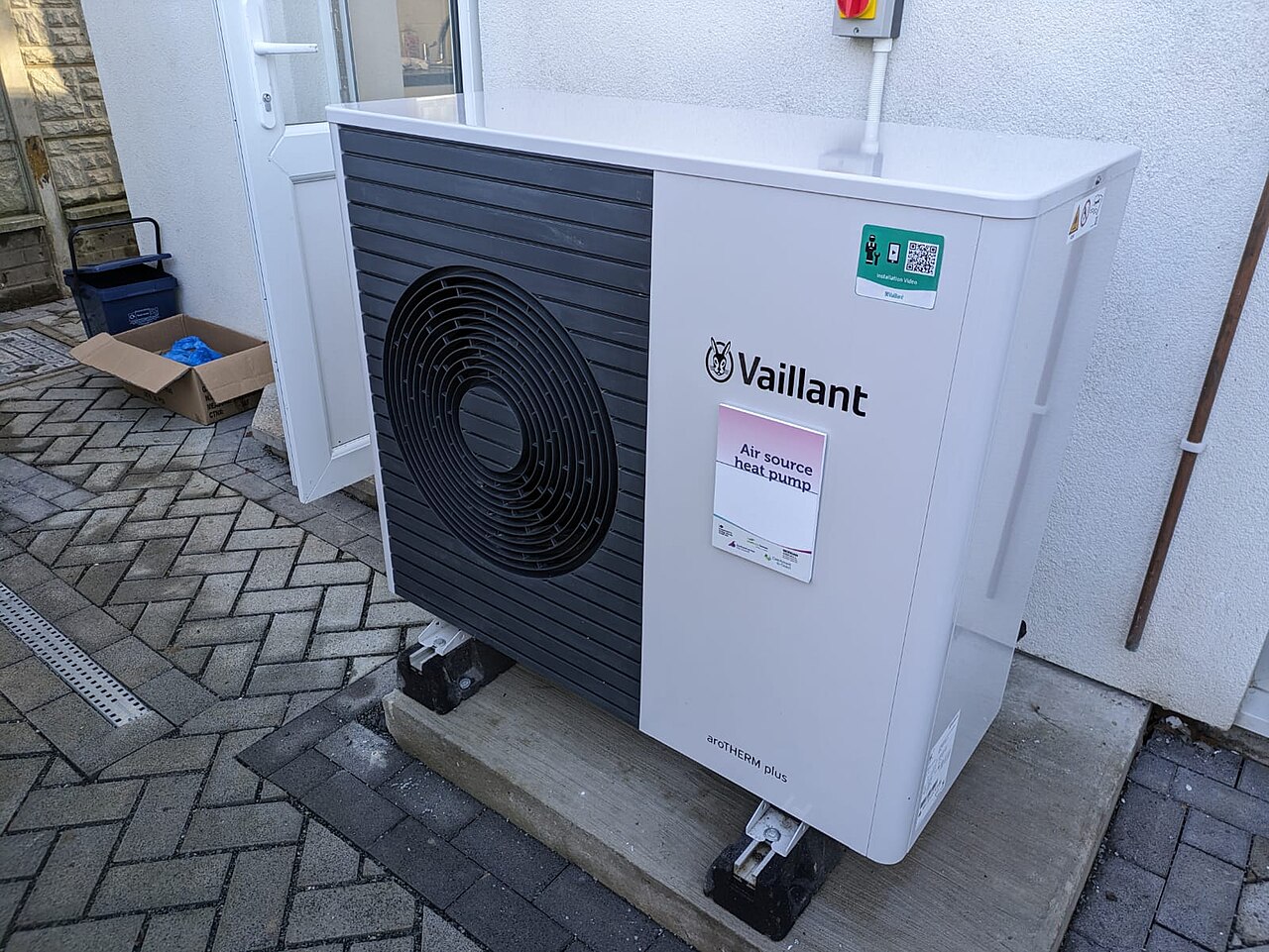 Unité extérieure de pompe à chaleur avec ventilateur, installée près d’un mur.