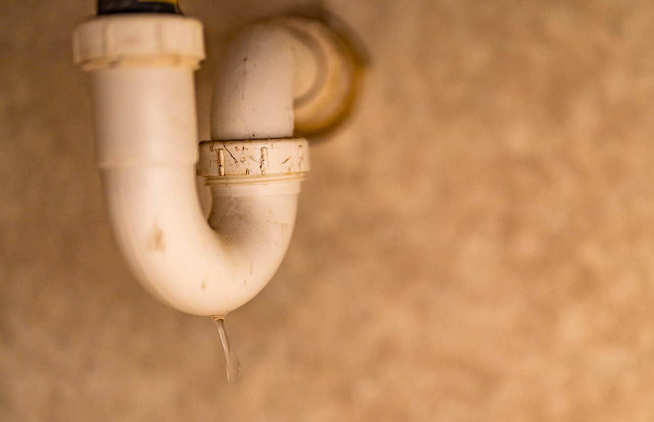Siphon en plastique et raccords d’évacuation visibles sous un lavabo.